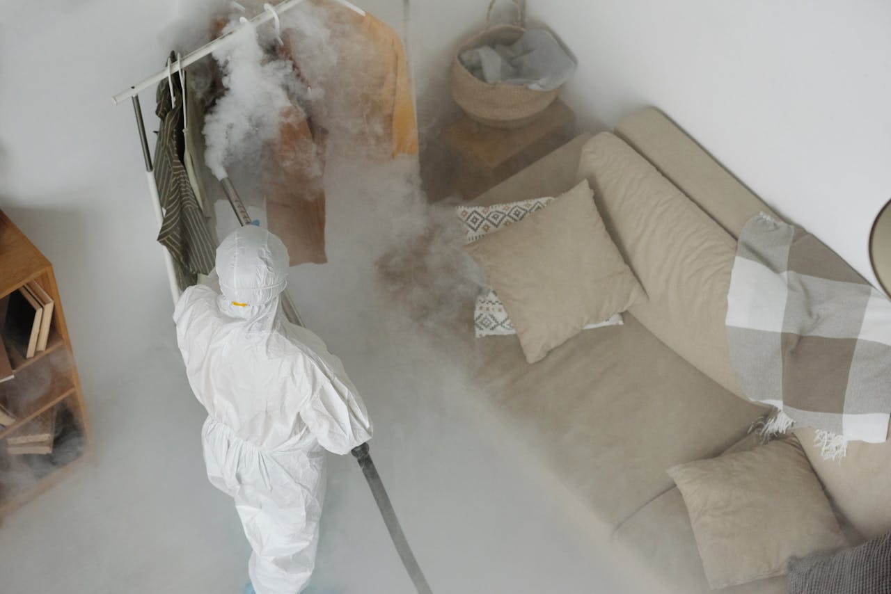 services-01 A worker in protective gear performs fumigation in a living room, using smoke to sanitize surfaces.